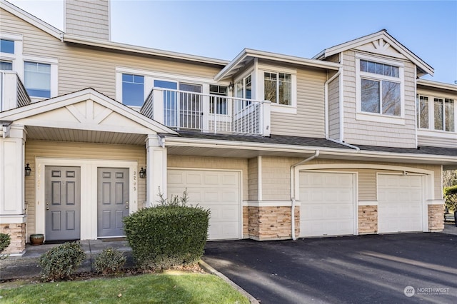 townhome / multi-family property featuring a shingled roof, a chimney, driveway, a balcony, and an attached garage