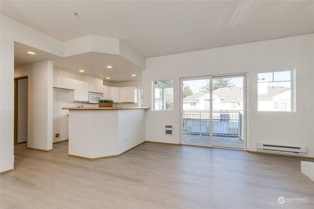 kitchen with white microwave, a peninsula, light wood-style floors, white cabinetry, and a baseboard radiator