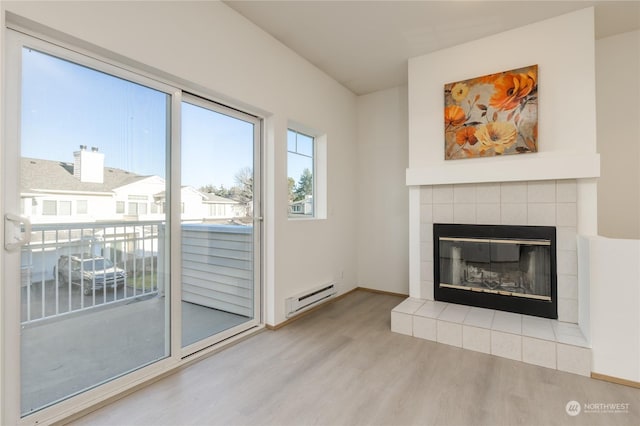 unfurnished living room with a tiled fireplace, a baseboard radiator, and light wood-type flooring