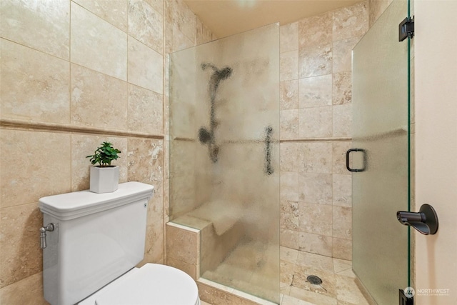 bathroom with a shower with door, tile walls, and toilet