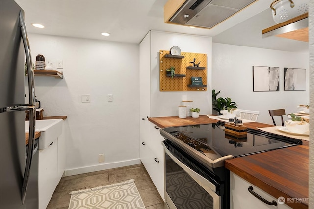 kitchen featuring butcher block counters, white cabinetry, light tile patterned floors, electric range, and stainless steel fridge