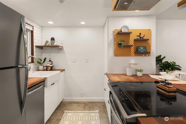 kitchen with light tile patterned flooring, appliances with stainless steel finishes, wood counters, white cabinetry, and sink