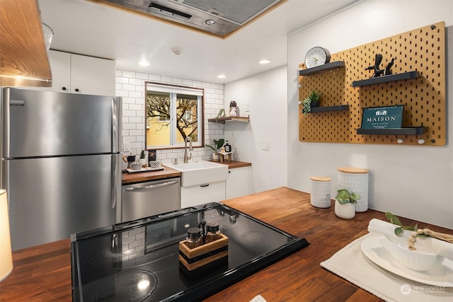 kitchen with sink, butcher block countertops, appliances with stainless steel finishes, white cabinetry, and backsplash