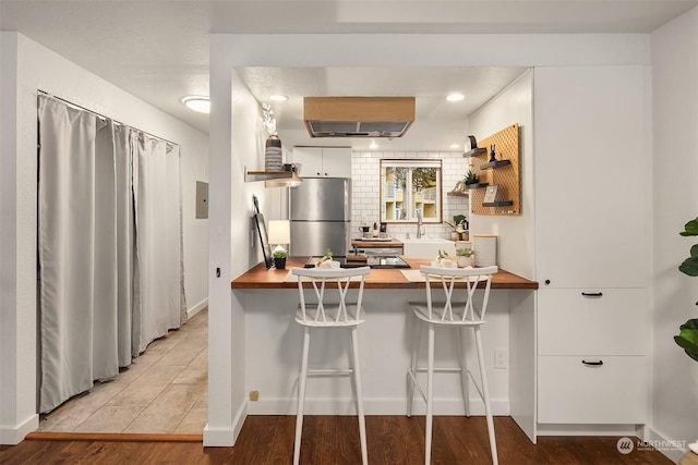 kitchen featuring stainless steel fridge, a breakfast bar area, wooden counters, white cabinetry, and kitchen peninsula