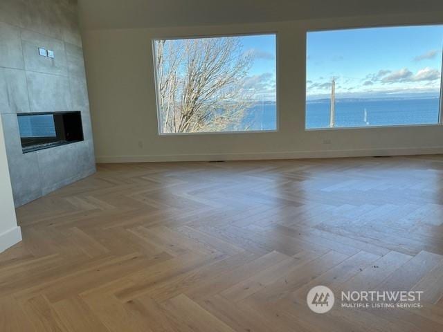 unfurnished living room featuring a water view, light parquet flooring, and a tile fireplace