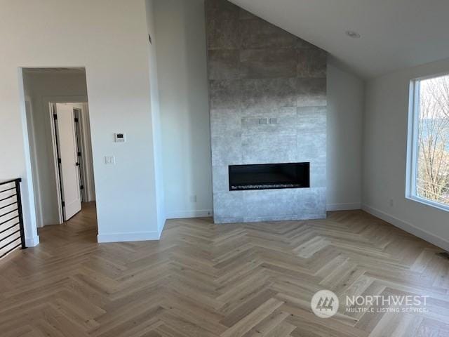 unfurnished living room with light parquet floors, high vaulted ceiling, and a fireplace