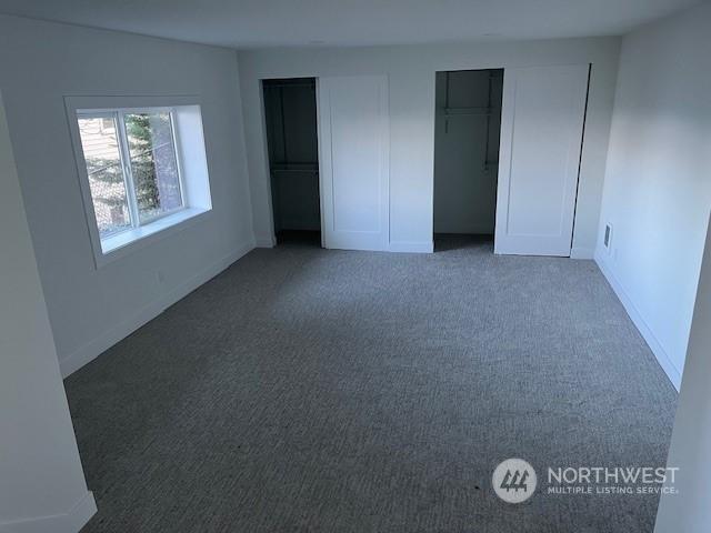 unfurnished bedroom featuring two closets and dark colored carpet