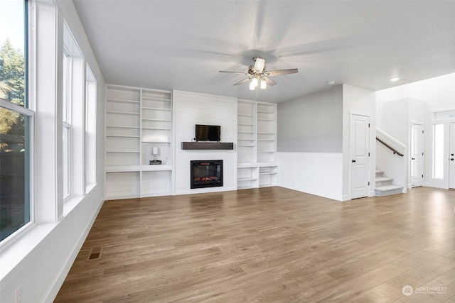 unfurnished living room with ceiling fan, a fireplace, and light wood-type flooring