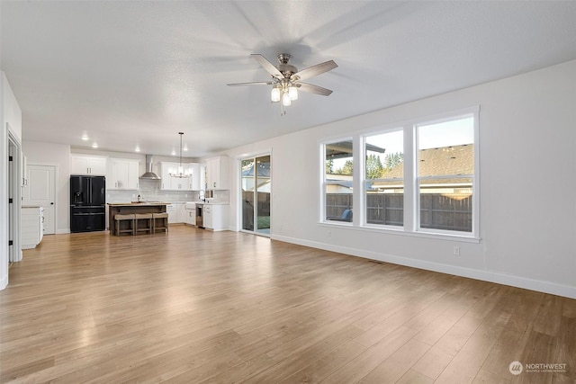 unfurnished living room featuring ceiling fan with notable chandelier and light hardwood / wood-style floors