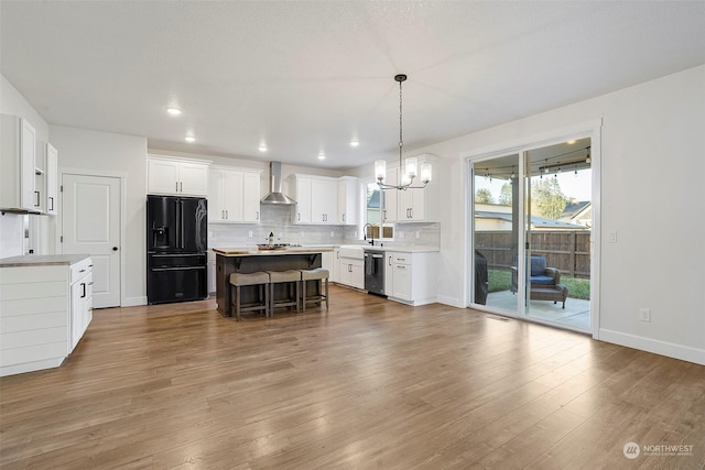 kitchen featuring white cabinets, black fridge, wall chimney exhaust hood, and a kitchen island