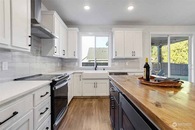 kitchen featuring stainless steel electric range oven, white cabinetry, wooden counters, plenty of natural light, and wall chimney range hood