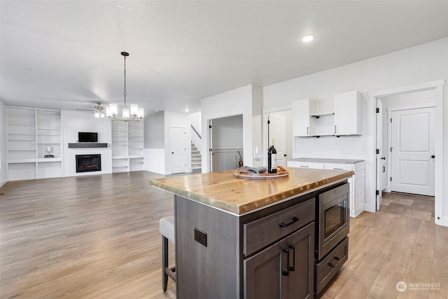 kitchen featuring pendant lighting, a kitchen breakfast bar, stainless steel microwave, white cabinets, and a kitchen island