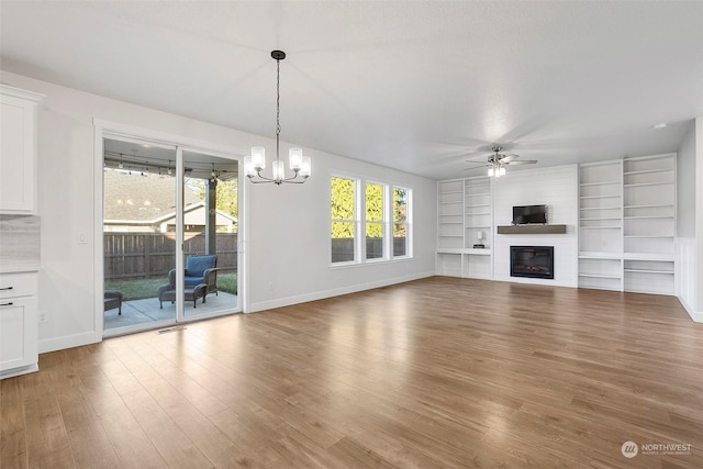 unfurnished living room featuring hardwood / wood-style flooring, ceiling fan with notable chandelier, and built in shelves