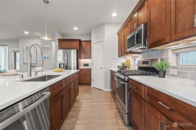 kitchen with appliances with stainless steel finishes, pendant lighting, tasteful backsplash, sink, and light hardwood / wood-style flooring