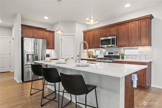 kitchen with hanging light fixtures, light wood-type flooring, stainless steel appliances, and a center island with sink