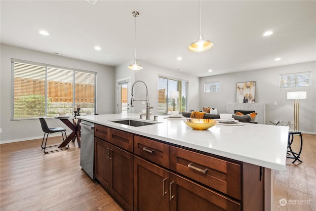 kitchen with sink, an island with sink, a kitchen bar, decorative light fixtures, and stainless steel dishwasher