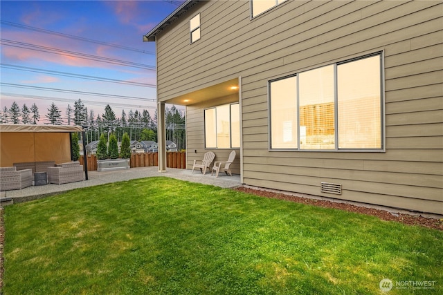 back of house at dusk with a yard, a patio area, visible vents, and fence