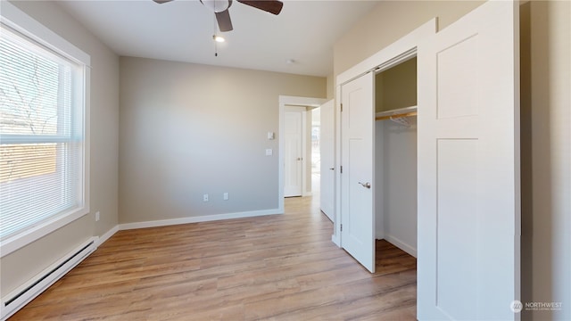 unfurnished bedroom with a closet, ceiling fan, baseboard heating, and light hardwood / wood-style floors