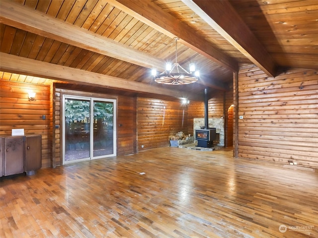 unfurnished living room with lofted ceiling with beams, wood-type flooring, a wood stove, a chandelier, and wooden ceiling