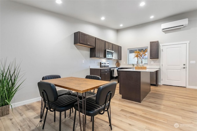 dining area with a towering ceiling, a wall unit AC, and light wood-type flooring