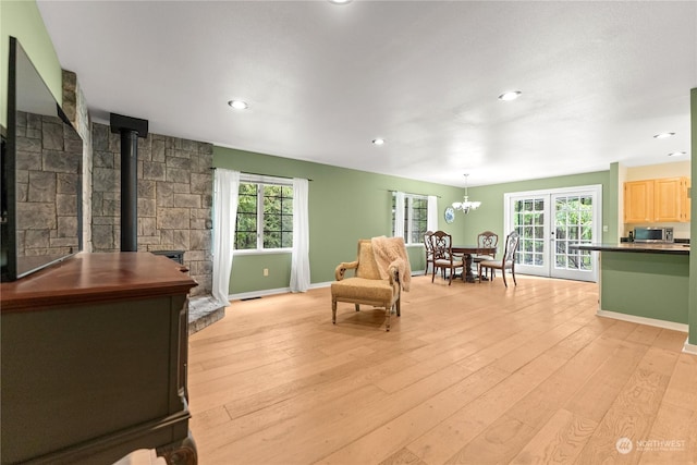 living area featuring french doors, a notable chandelier, light hardwood / wood-style floors, and a wood stove