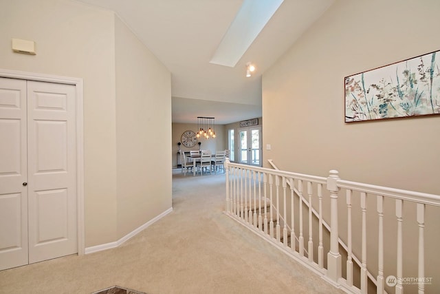 corridor with vaulted ceiling with skylight, light colored carpet, and a notable chandelier