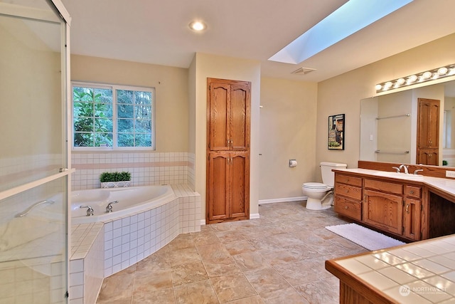 bathroom featuring a relaxing tiled tub, vanity, a skylight, and toilet