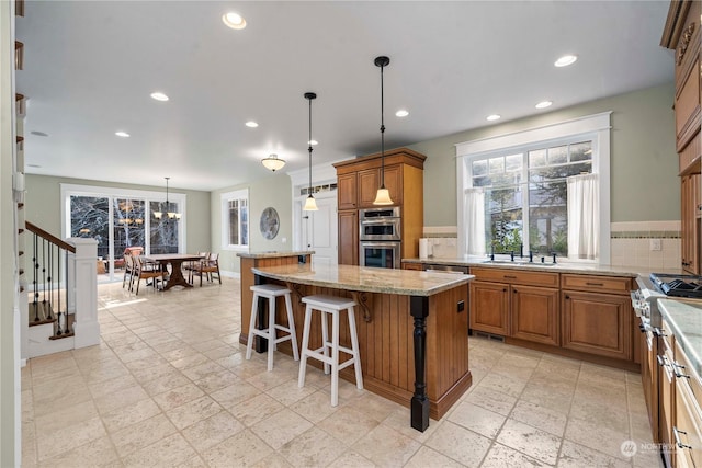 kitchen with a breakfast bar, stainless steel appliances, a center island, light stone countertops, and decorative light fixtures