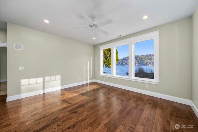 empty room featuring a water view, ceiling fan, and dark hardwood / wood-style flooring