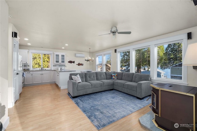 living room with a wall unit AC, sink, ceiling fan with notable chandelier, and light hardwood / wood-style flooring