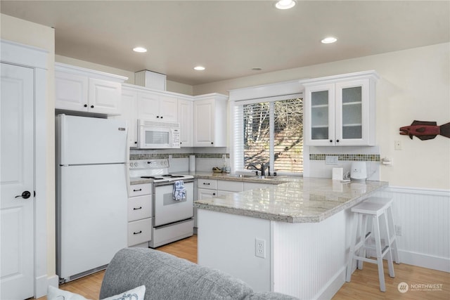 kitchen with white appliances, kitchen peninsula, light hardwood / wood-style floors, and white cabinets