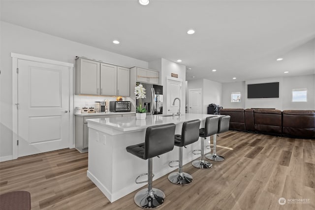 kitchen with a kitchen bar, sink, a center island with sink, light wood-type flooring, and stainless steel fridge