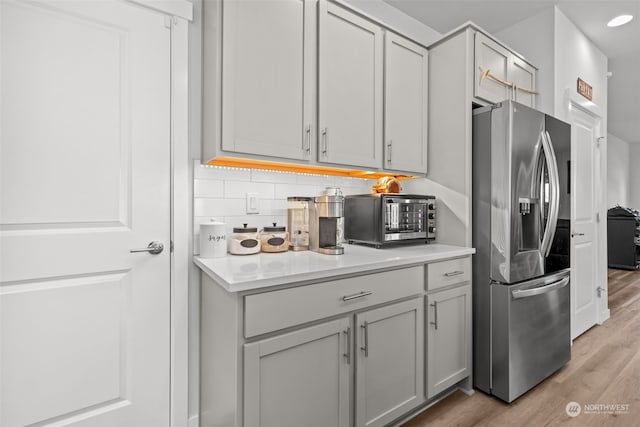 kitchen with stainless steel refrigerator with ice dispenser, light hardwood / wood-style flooring, decorative backsplash, and gray cabinetry