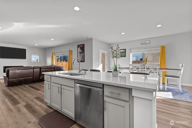 kitchen featuring sink, light hardwood / wood-style flooring, stainless steel dishwasher, and an island with sink