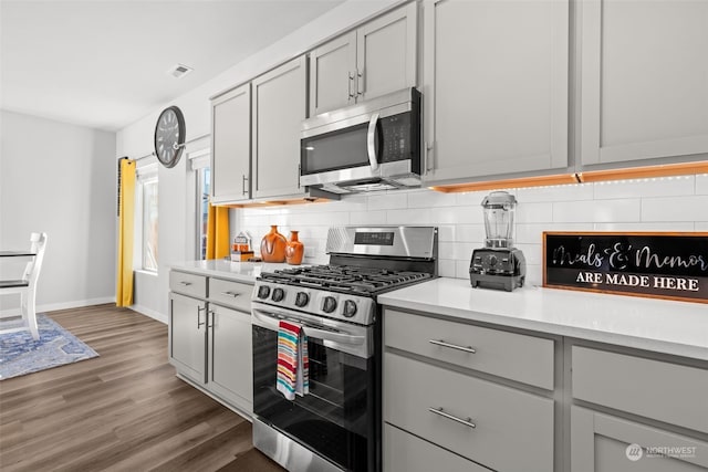 kitchen with stainless steel appliances, gray cabinets, dark wood-type flooring, and decorative backsplash