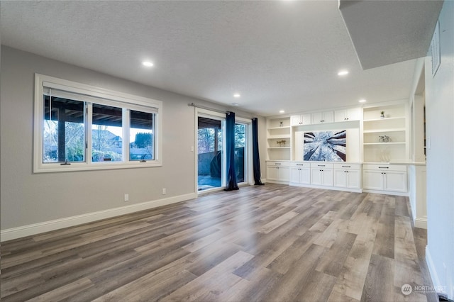 unfurnished living room featuring built in shelves, a textured ceiling, and light wood-type flooring