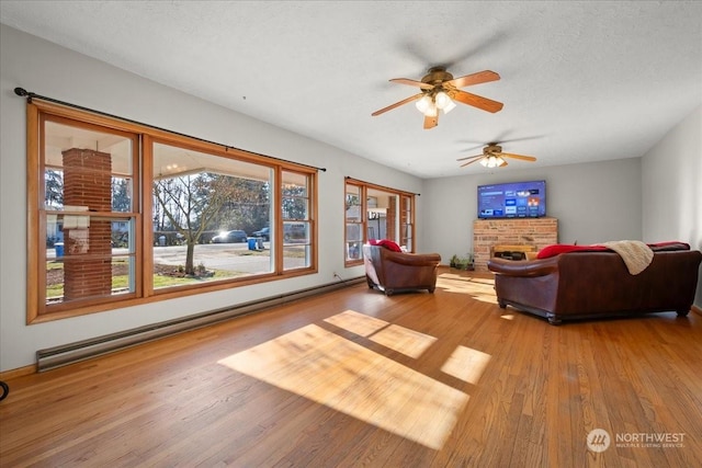 living room featuring a fireplace, hardwood / wood-style flooring, a baseboard heating unit, ceiling fan, and a textured ceiling