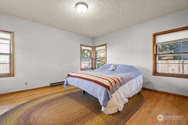 bedroom featuring a baseboard heating unit, hardwood / wood-style floors, and a textured ceiling