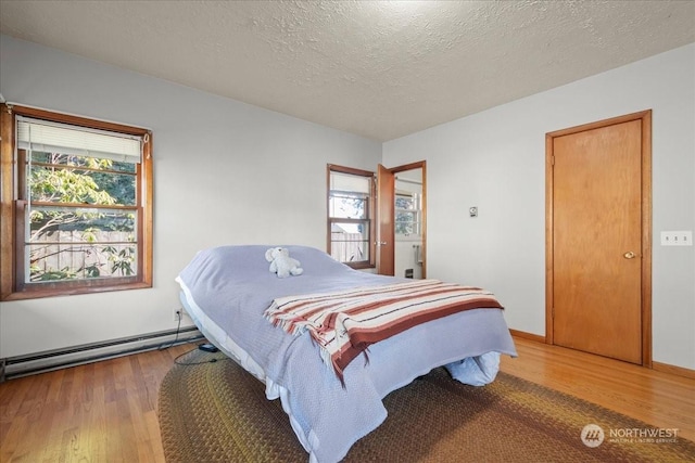 bedroom with a baseboard heating unit, wood-type flooring, and a textured ceiling