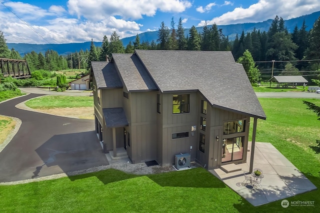 exterior space featuring ac unit, a lawn, a mountain view, board and batten siding, and roof with shingles