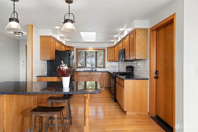 kitchen featuring hanging light fixtures, a skylight, black appliances, and sink