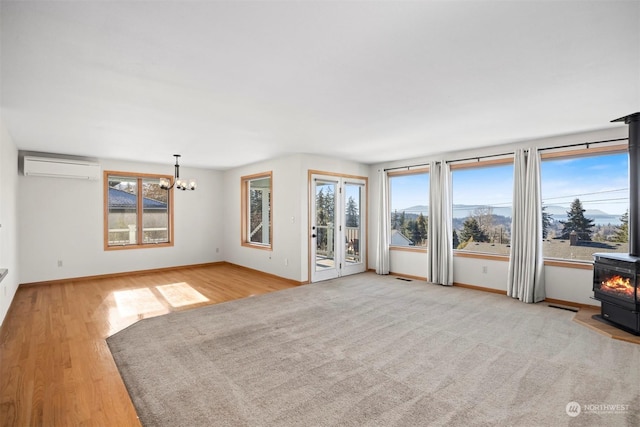 unfurnished living room featuring a notable chandelier, a wall mounted air conditioner, light hardwood / wood-style floors, and a wood stove