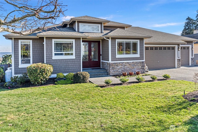 view of front of home with driveway, stone siding, roof with shingles, an attached garage, and a front yard