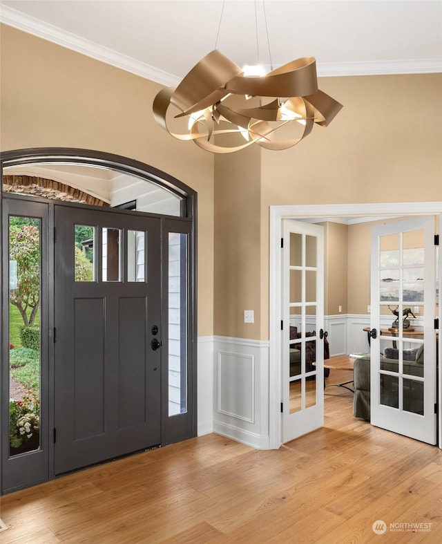 foyer entrance featuring french doors, crown molding, a chandelier, and light hardwood / wood-style floors