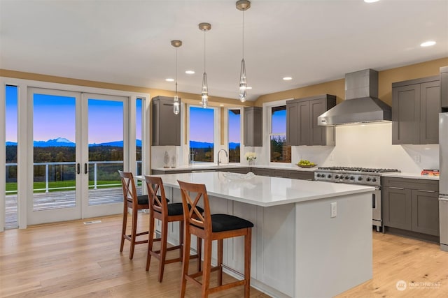 kitchen featuring stainless steel range, wall chimney exhaust hood, hanging light fixtures, and a kitchen island