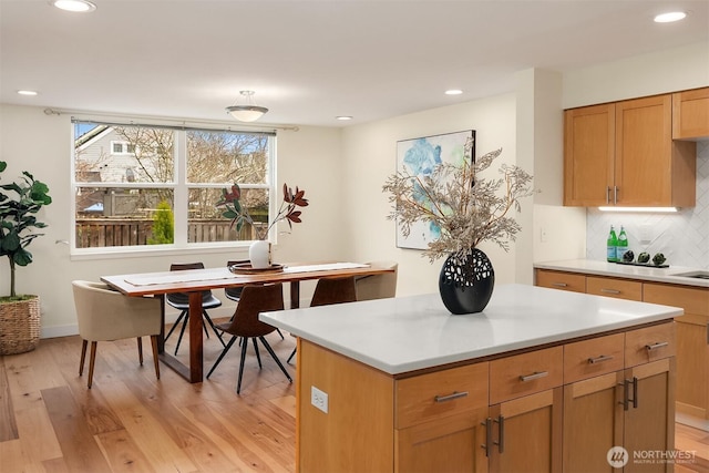 kitchen featuring light wood finished floors, backsplash, a center island, recessed lighting, and light countertops