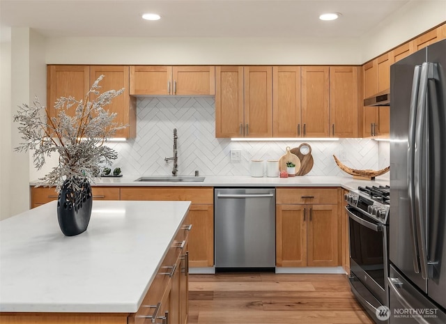 kitchen with a sink, stainless steel appliances, brown cabinetry, and light countertops