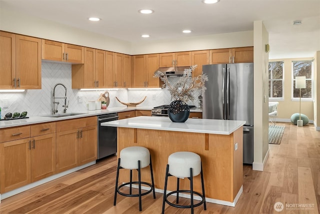 kitchen with a breakfast bar area, a sink, stainless steel appliances, light countertops, and under cabinet range hood