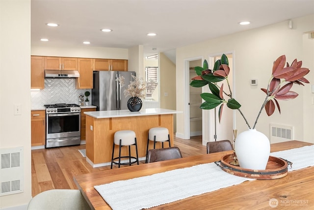 kitchen featuring light countertops, under cabinet range hood, appliances with stainless steel finishes, tasteful backsplash, and a center island