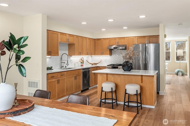 kitchen with a center island, under cabinet range hood, light countertops, stainless steel appliances, and a sink